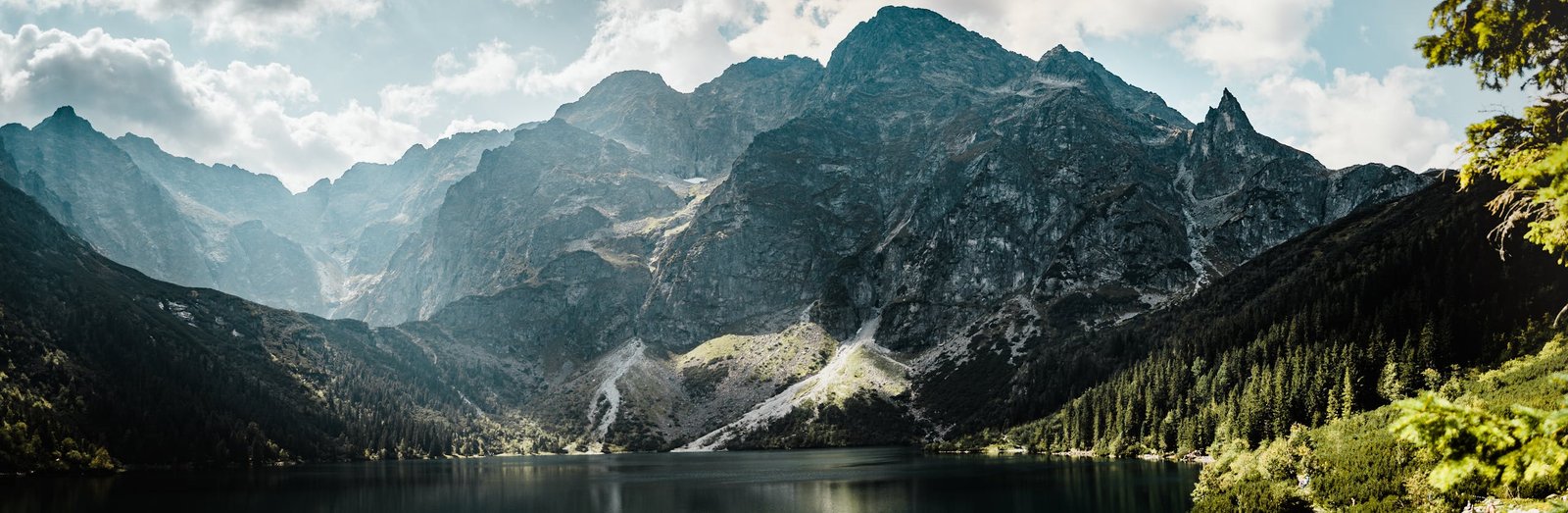 Serene mountain lake scene with rugged peaks and forested valleys under a bright day sky.
